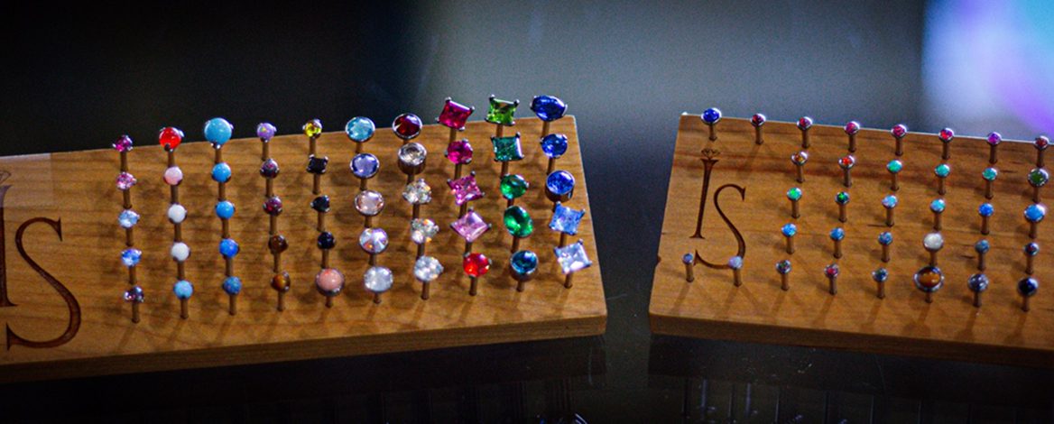 Rows of colorful gemstone stud earrings are displayed on two wooden boards with the letters "J" and "S" engraved on them.